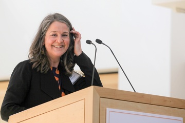Woman with light skin tone standing behind a podium and smiling.